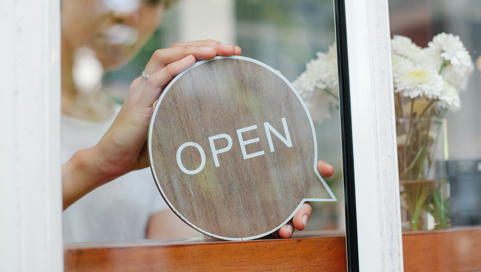 crop barista putting signboard with open inscription on glass wall